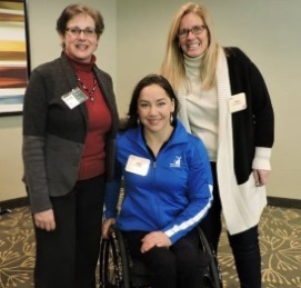 Three smiling women, one seated in a wheelchair.
