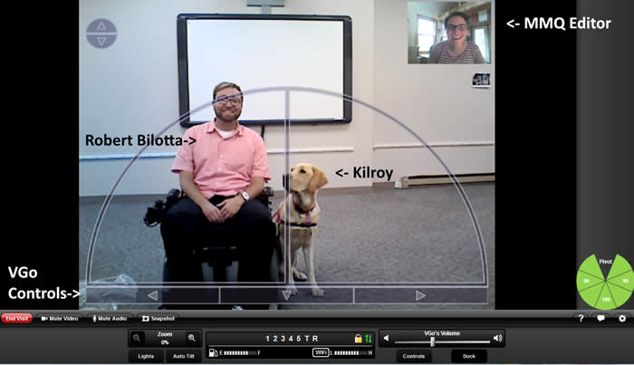 A screen shot showing a smiling man seated in a wheelchair flanked by his service dog. The image is framed by VGo app controls. In the upper right corner is the smiling image of a woman, the VGo's driver. There is a smart board mounted on the wall behind the man. 