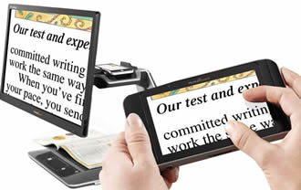 Desktop video magnifier displaying large text and cradeling hand-held video magnifier. Hand-held device also in foreground displaying same captured text.