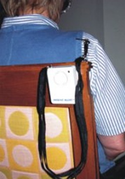 Alarm attached to back of wheelchair with cord and pin attached to seated user's clothing