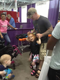Adleigh Cucovatz tries out the Upsee with her dad. The device allows her to be strapped to her father, yet walk along assisted at ground level height. 