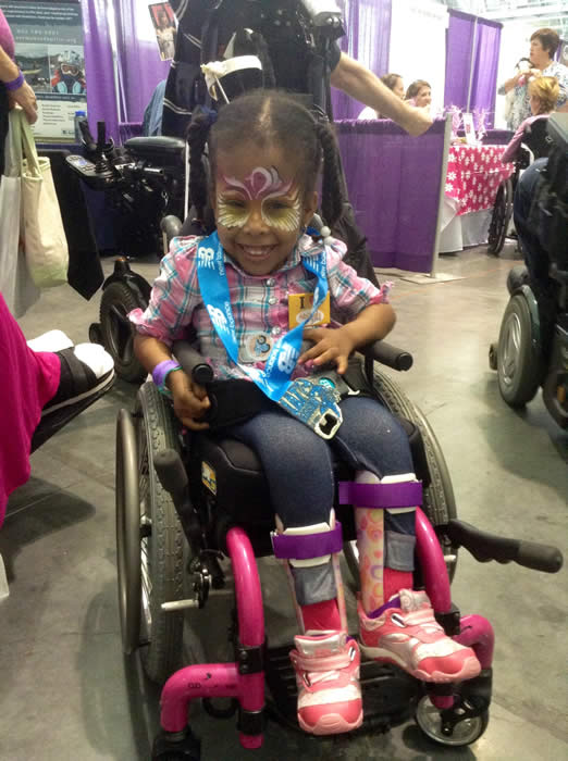 Small girl with painted face smiling in her wheelchair. 