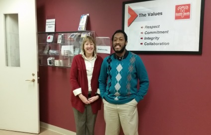 A woman and a man standing and smiling beneath a sign that lists Easter Seals values: Respect, commitment, integrity, collaboration.