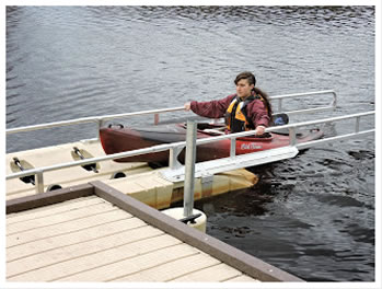 A woman seated in a kayak is exiting the water using the EZ dock launch system, pulling herself on the side rails up the chute to the dock. 