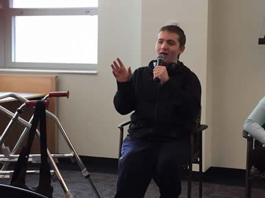 Seated male student speaks into a mic. Walker is next to him. 