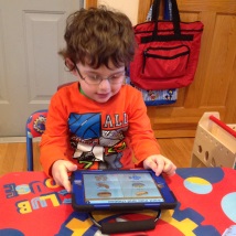 Young boy seated holding and looking at a tablet displaying picture icons.
